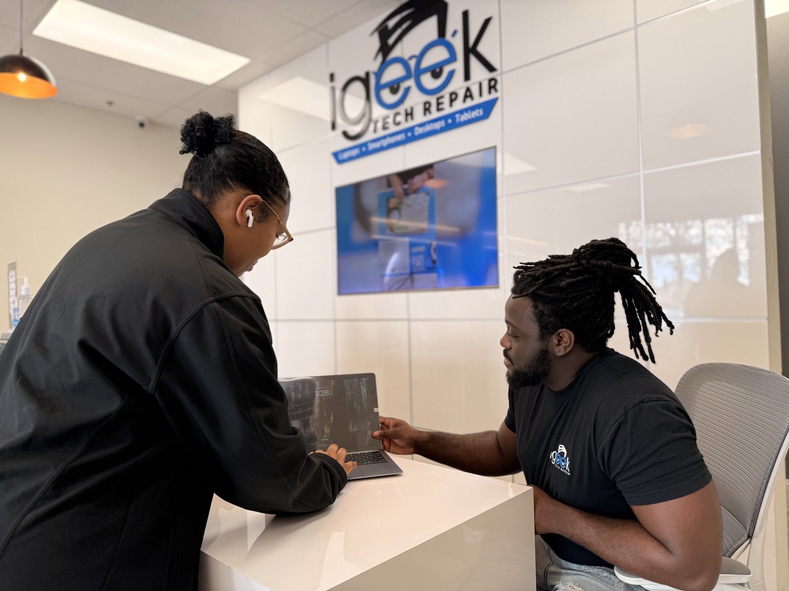 An iGeek technician walking a customer through a laptop repair at the counter