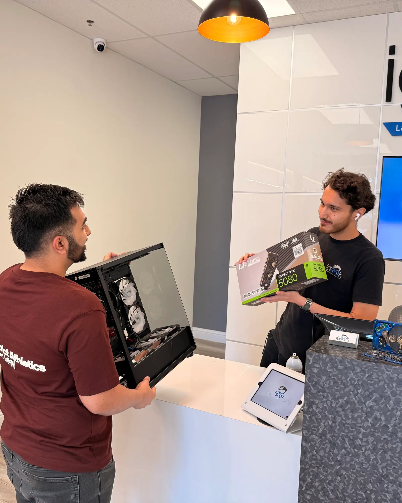 Technician showing a graphics card box beside an open custom PC at the counter