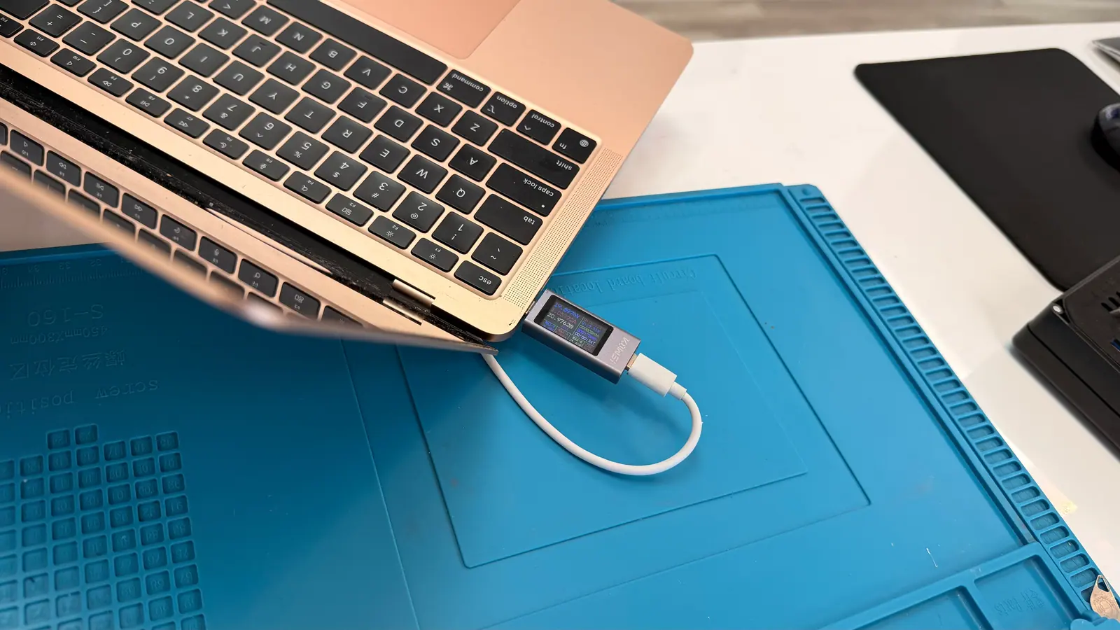 A laptop on the bench with a USB-C power meter inline on its charging cable