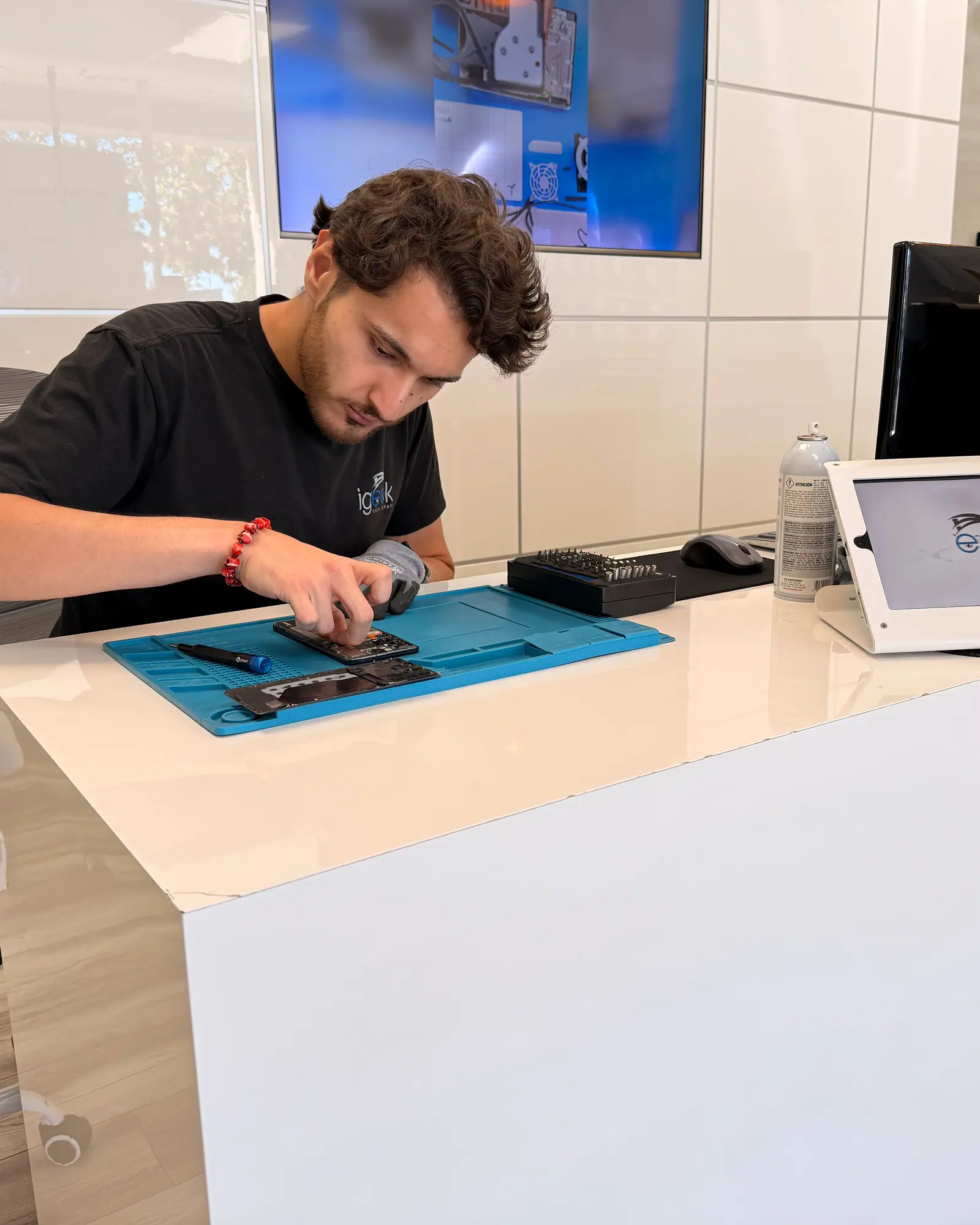 A technician working on a dismantled phone at the counter bench with the lobby behind